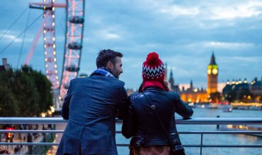 two tourists overlooking river Thames with view of London Eye and Big Ben